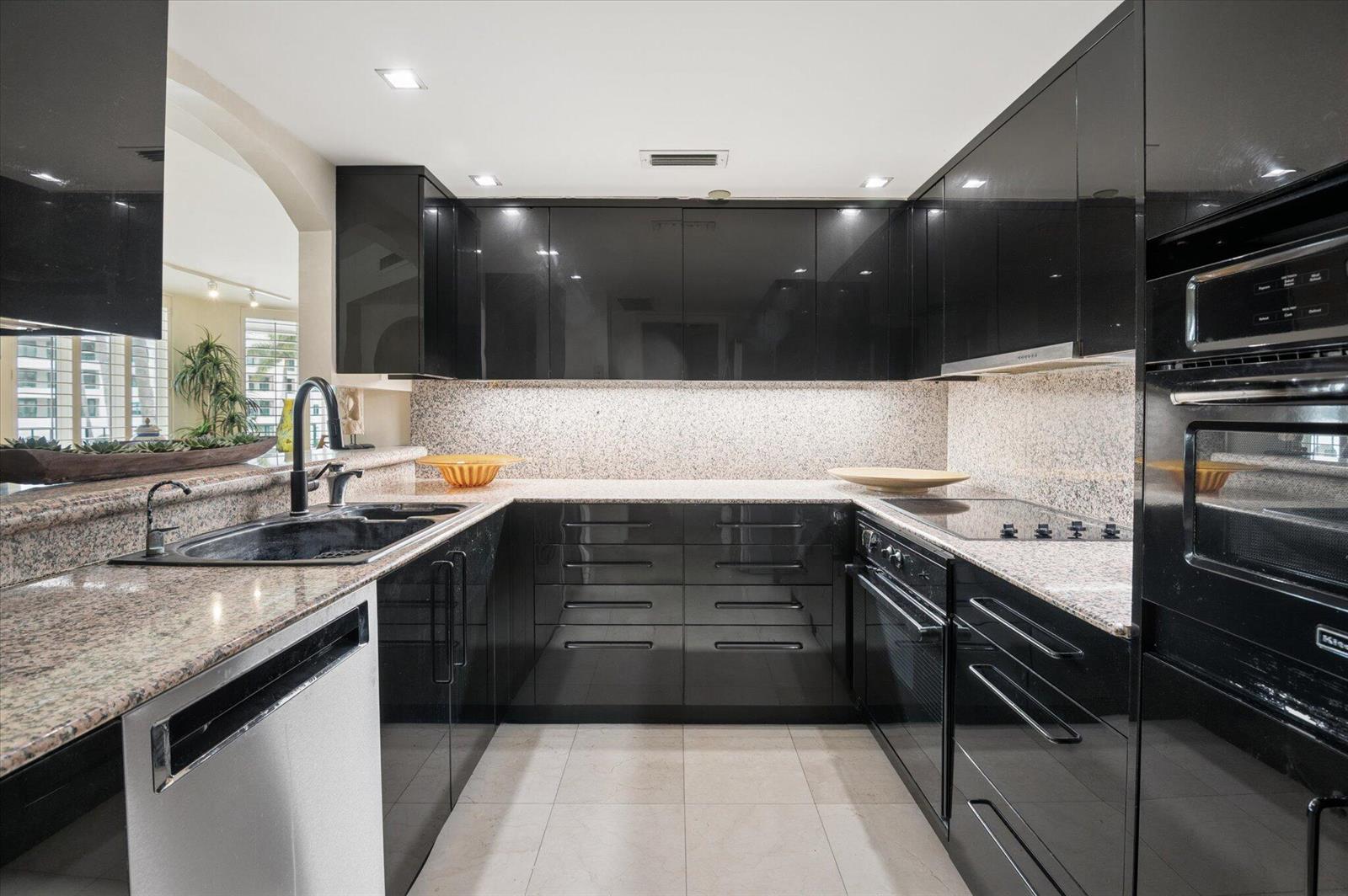A modern kitchen features black high-gloss cabinets, granite countertops, and stainless steel appliances — 120 SE 5th Avenue # 329, Boca Raton FL 33432, BOCA RATON, FL