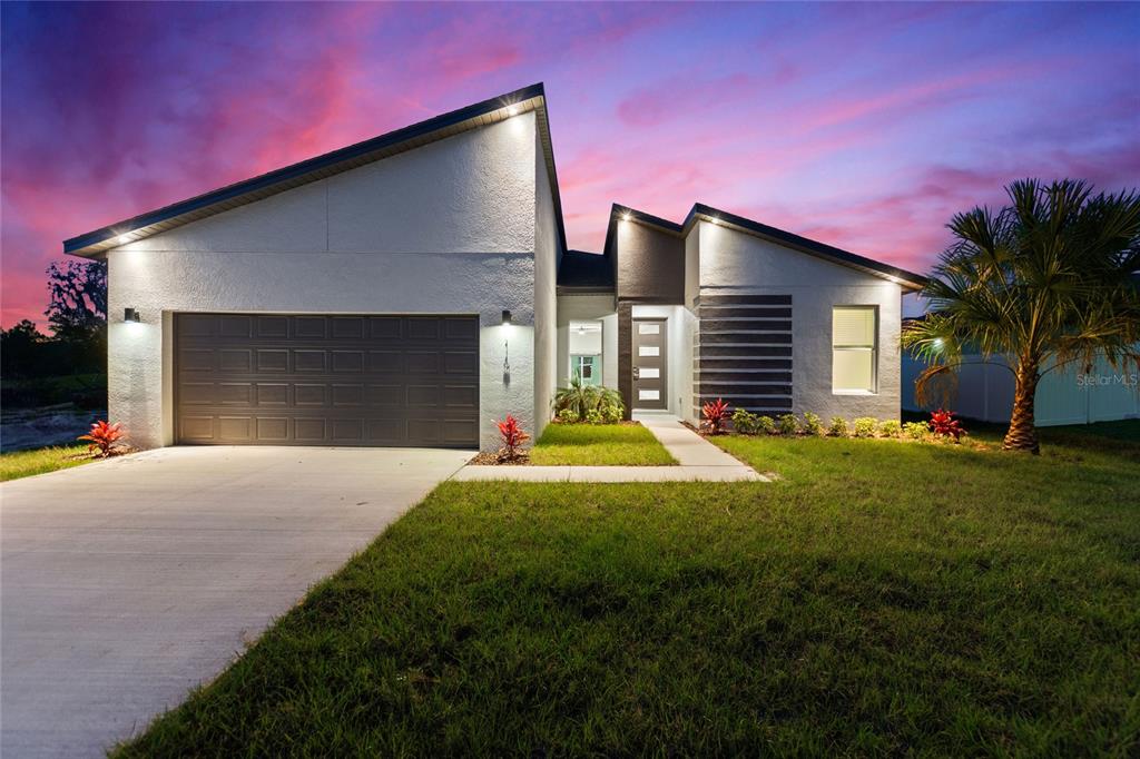 A modern single-story house with a two-car garage at dusk under a vibrant sky — 119 TULIP LANE, KISSIMMEE, FL