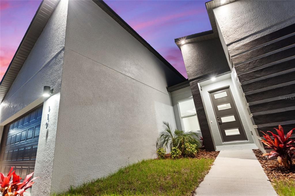 A modern house exterior features a gray stucco facade, a dark front door, and garage — 119 TULIP LANE, KISSIMMEE, FL