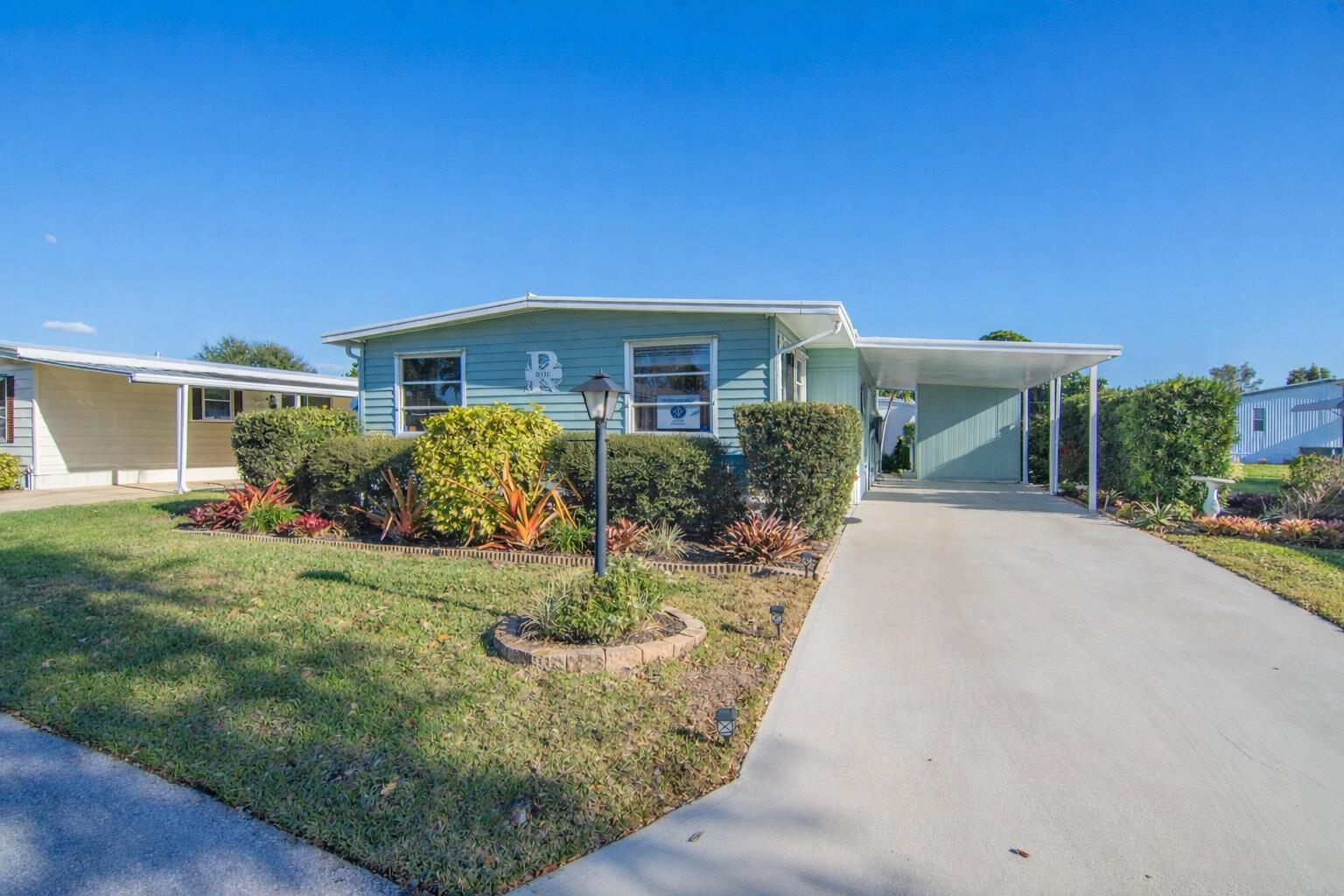 A light blue single-story manufactured home features a concrete driveway and a covered carport — 485 Onyx Way, Jensen Beach FL 34957, JENSEN BEACH, FL