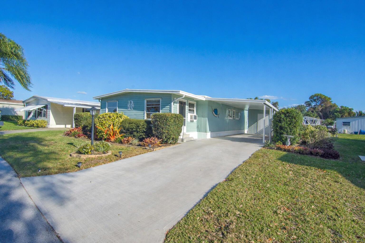 A light green manufactured home with a concrete driveway and a covered carport — 485 Onyx Way, Jensen Beach FL 34957, JENSEN BEACH, FL