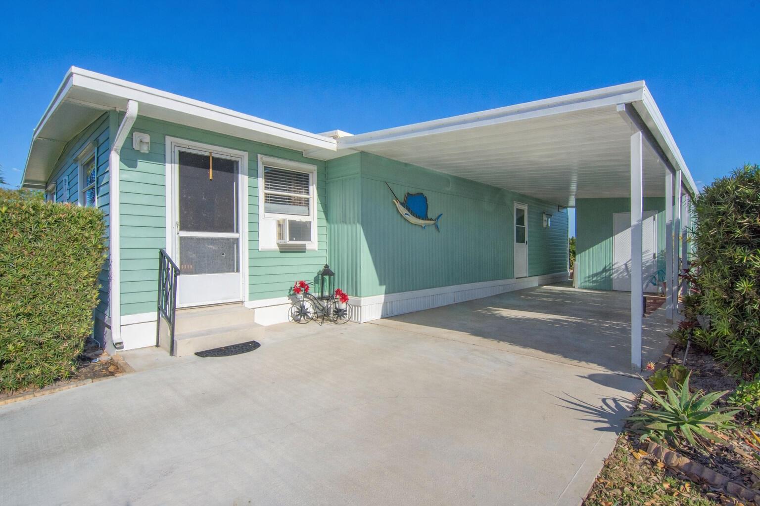 A light green mobile home features a concrete driveway, a carport, and a sailfish wall decoration — 485 Onyx Way, Jensen Beach FL 34957, JENSEN BEACH, FL