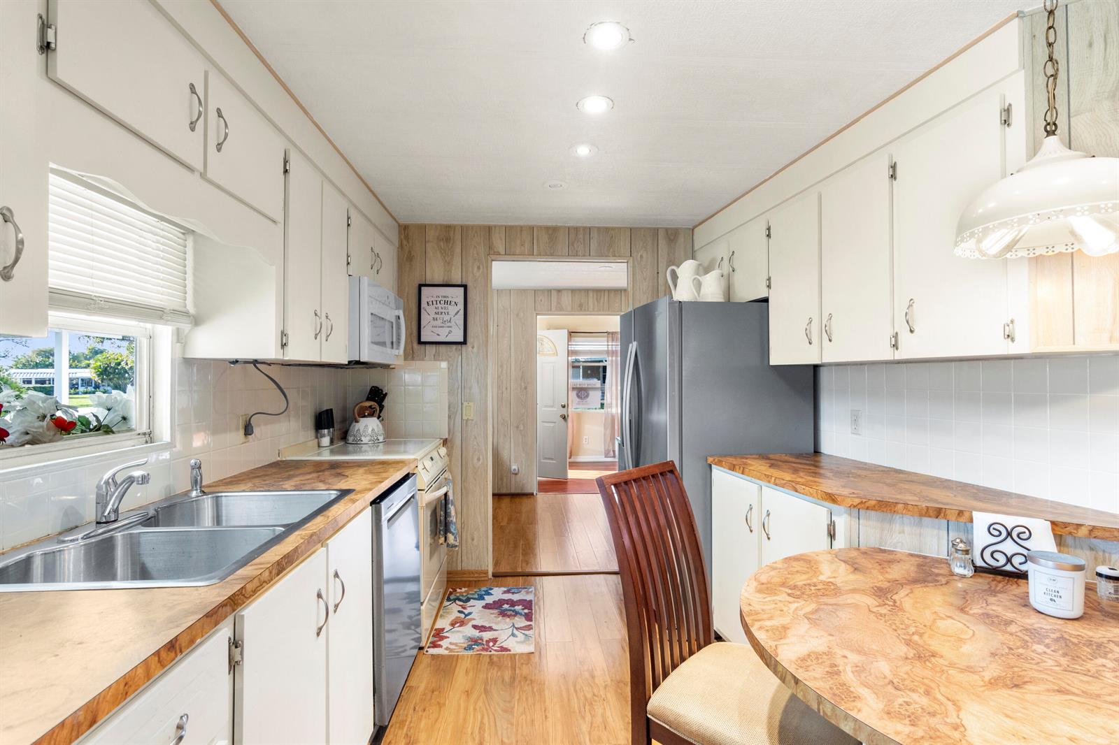 A galley kitchen features white cabinets, wood-look countertops, a stainless steel refrigerator, and wood paneling — 485 Onyx Way, Jensen Beach FL 34957, JENSEN BEACH, FL