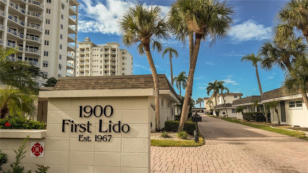 A stone sign for a residential complex stands before a palm-lined paved driveway — 1900 BENJAMIN FRANKLIN DRIVE UNIT 201BER, SARASOTA, FL