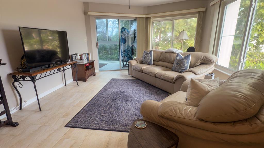 A living room features beige leather sofas, a dark area rug, and sliding glass doors — 1900 BENJAMIN FRANKLIN DRIVE UNIT 201BER, SARASOTA, FL