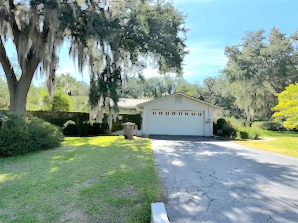 A single-story house with a white garage door sits behind a driveway and large trees — 2143 SE 3RD STREET, OCALA, FL