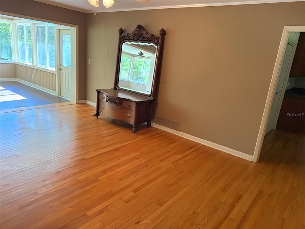 A living room with hardwood floors, a large antique mirror, and an adjacent sunroom — 2143 SE 3RD STREET, OCALA, FL