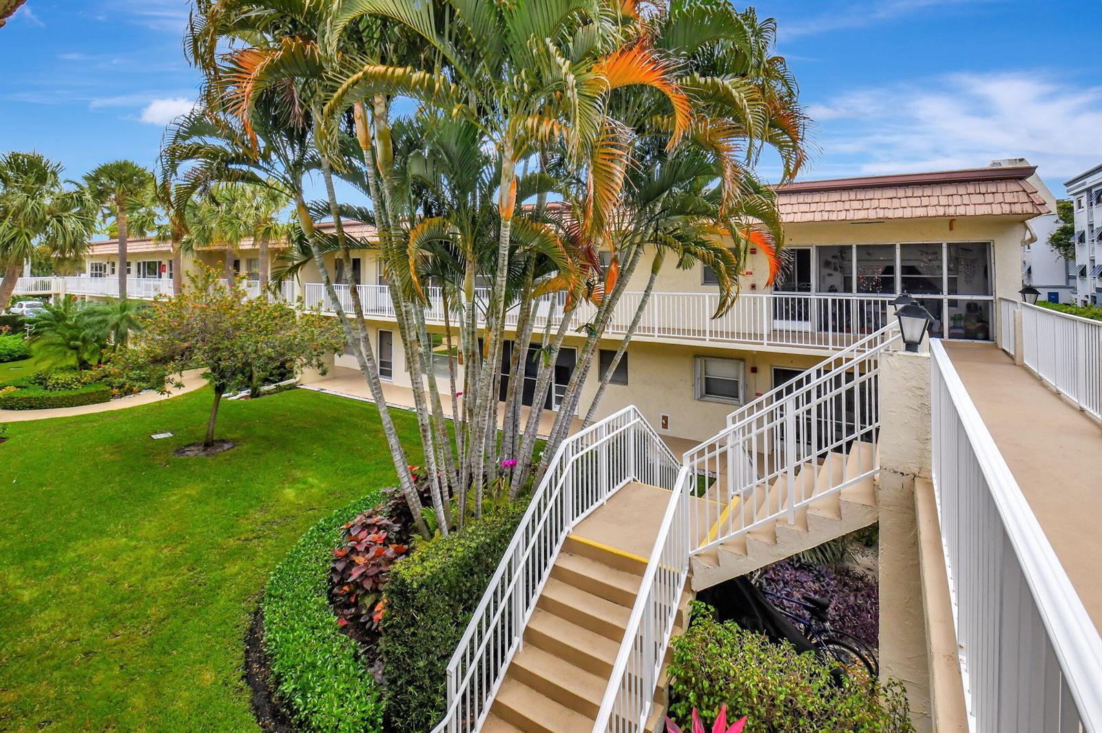 An exterior view of a multi-story apartment building with a staircase, walkway, and palm trees — 638 Snug Harbor Drive # E11, Boynton Beach FL 33435, BOYNTON BEACH, FL