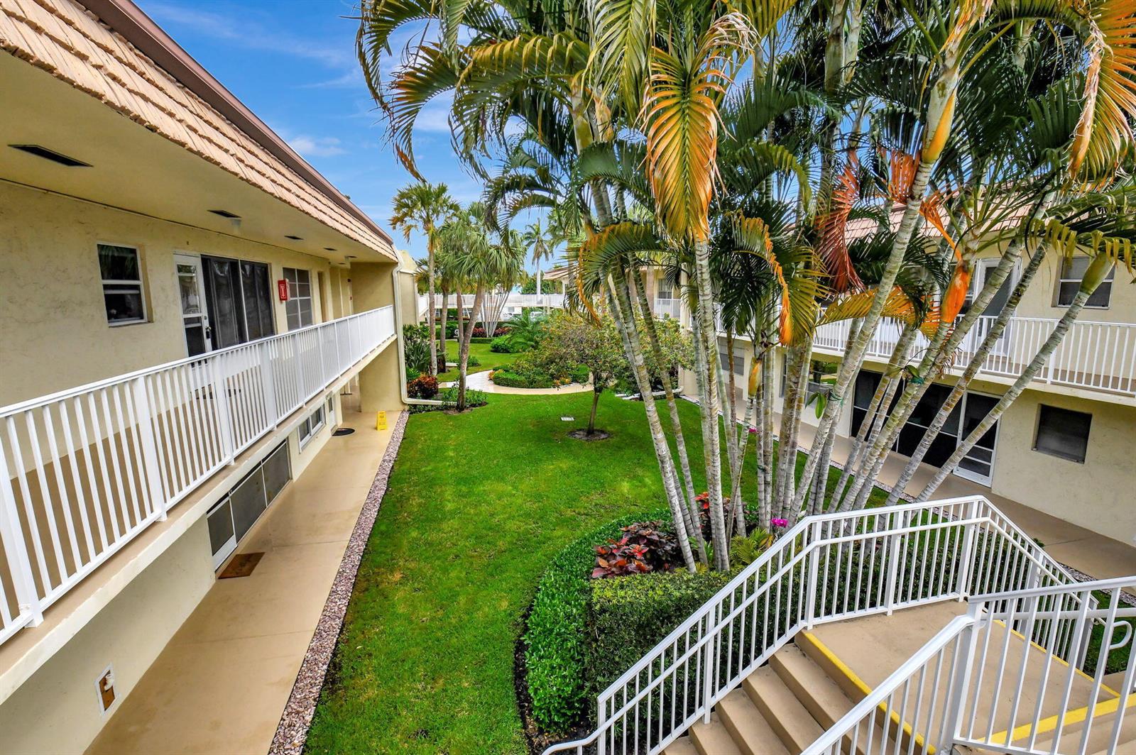 An exterior view of a multi-story apartment complex with a central courtyard and palm trees — 638 Snug Harbor Drive # E11, Boynton Beach FL 33435, BOYNTON BEACH, FL