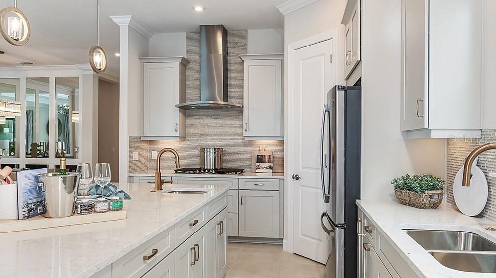A modern kitchen features light gray cabinets, white countertops, stainless steel appliances, and pendant lighting — 3220 VICENZA COURT, BRADENTON, FL