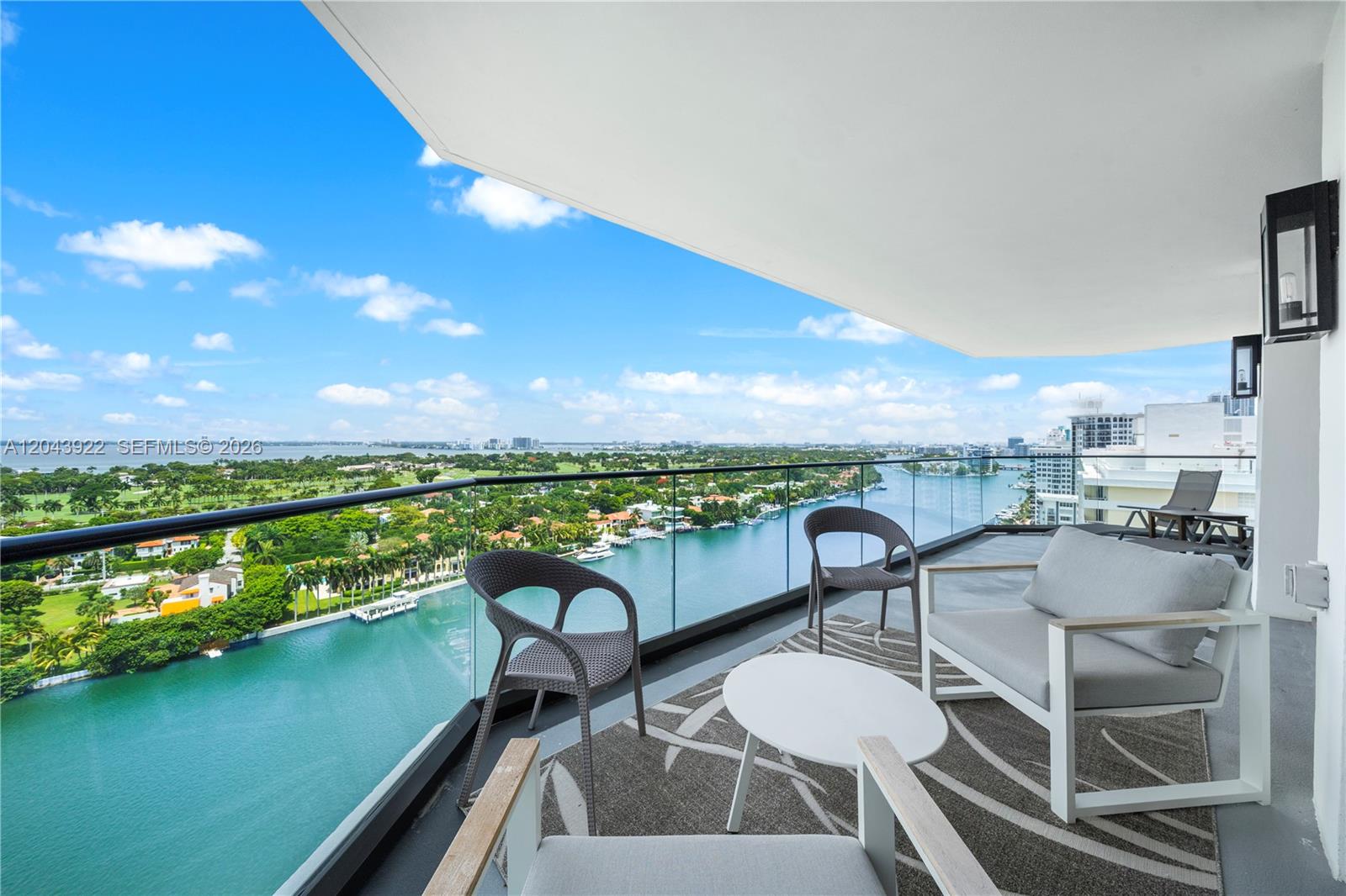A balcony with outdoor furniture overlooks a waterway, a golf course, and a city skyline — 5500 Collins Ave # 1902, Miami Beach FL 33140, MIAMI BEACH, FL