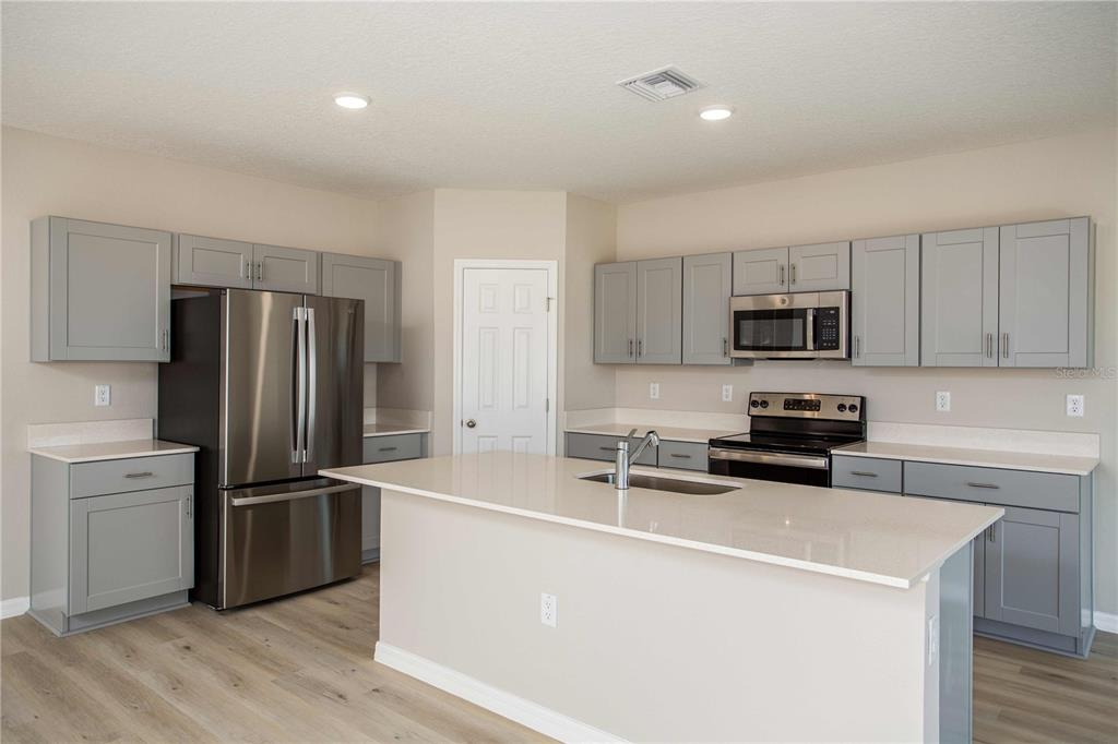 A kitchen features gray shaker cabinets, stainless steel appliances, and a central quartz-topped island — 36628 SAGEMOOR DRIVE, ZEPHYRHILLS, FL
