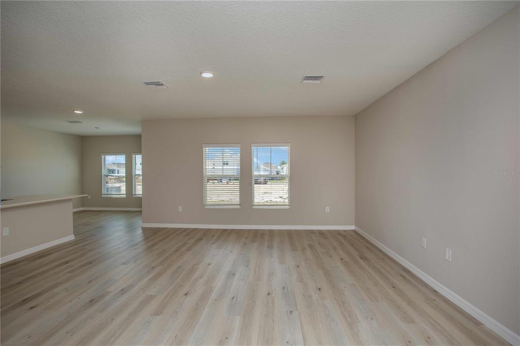 An empty living room features light wood-look flooring, beige walls, and two windows — 36628 SAGEMOOR DRIVE, ZEPHYRHILLS, FL