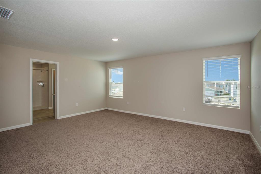 A carpeted bedroom features neutral walls, two windows, and a doorway leading to a bathroom — 36628 SAGEMOOR DRIVE, ZEPHYRHILLS, FL