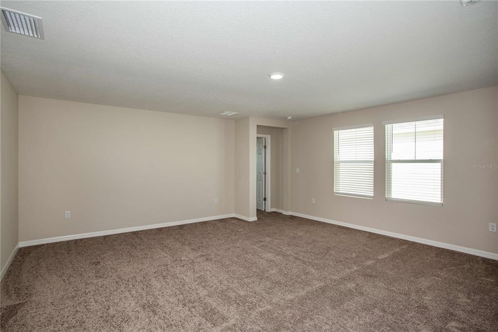 An empty room features beige walls, brown carpeting, two windows with blinds, and a doorway — 36628 SAGEMOOR DRIVE, ZEPHYRHILLS, FL