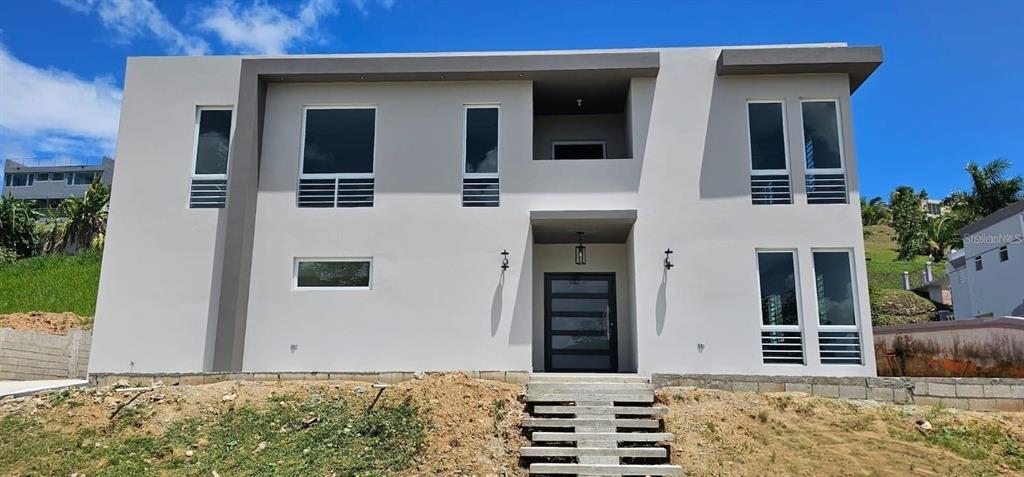A modern two-story house with a gray exterior, large windows, and a central front entrance — D-26 MANSIONES PLAYA HUCARES UNIT D-26, NAGUABO, PR