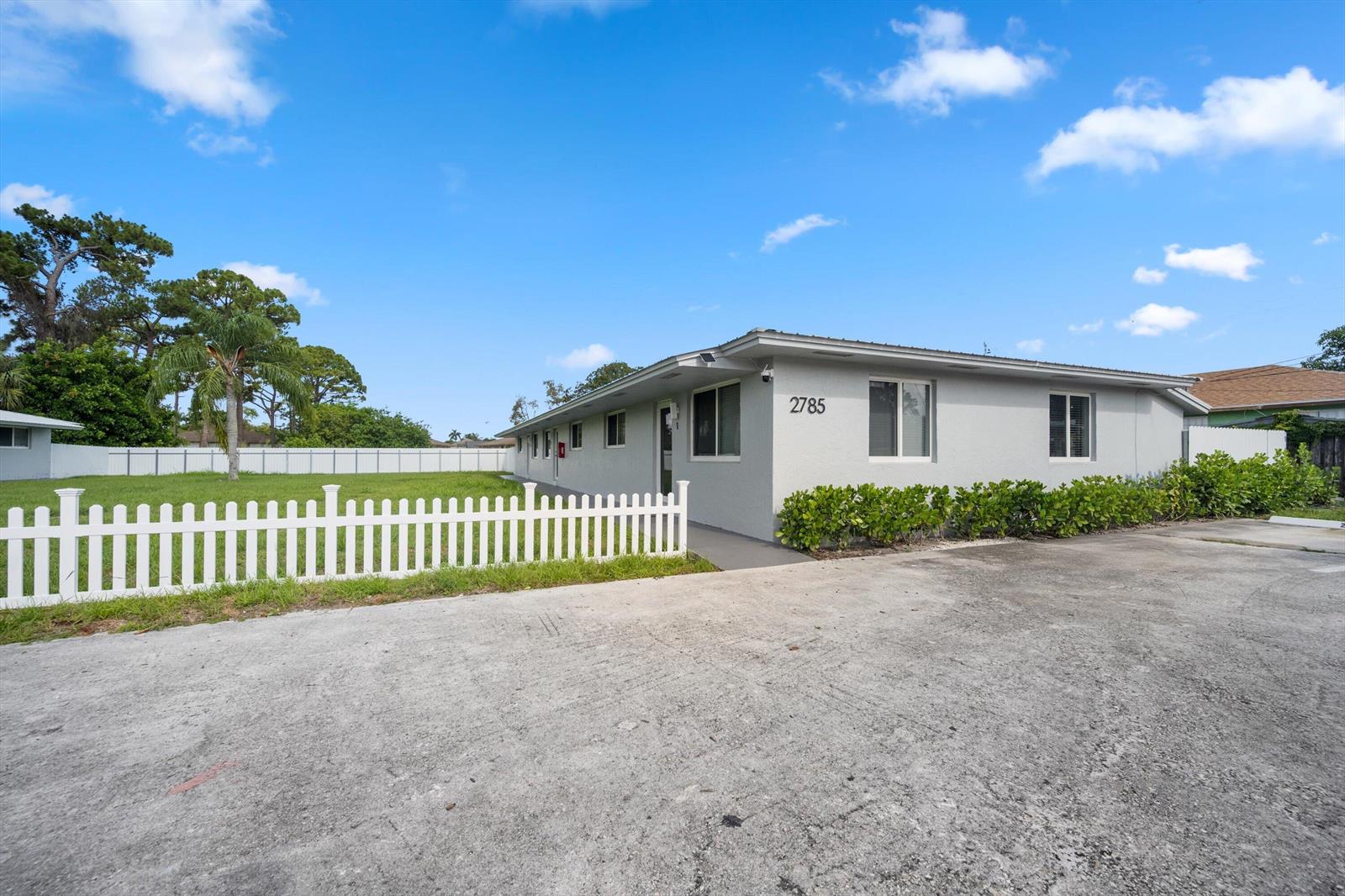 A single-story gray building with a white picket fence and a concrete parking area — 2807 Reo Lane # 1, Palm Springs FL 33461, PALM SPRINGS, FL