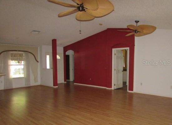 A spacious living room features light wood flooring, a vaulted ceiling, and two palm-leaf ceiling fans — 1142 MEADOWBEND DRIVE, LEESBURG, FL