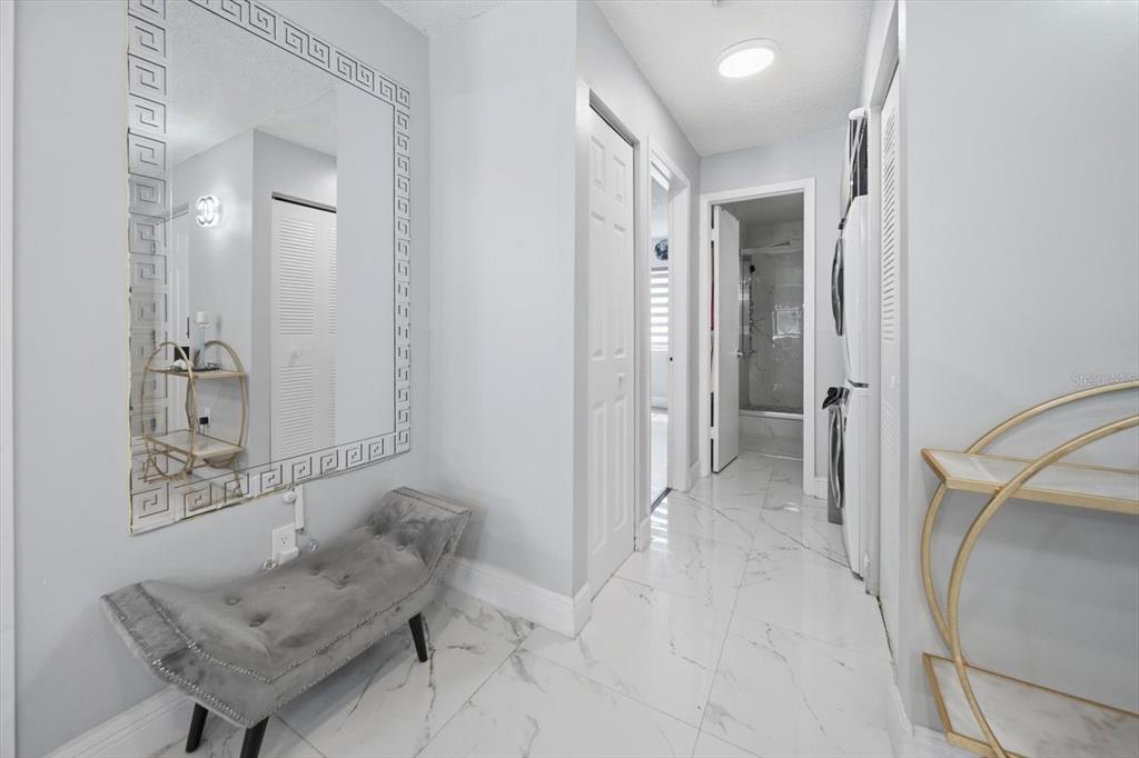 A hallway features white marble-look tile flooring, a large decorative mirror, and a grey bench — 11566 7TH LANE N UNIT 1208, ST PETERSBURG, FL