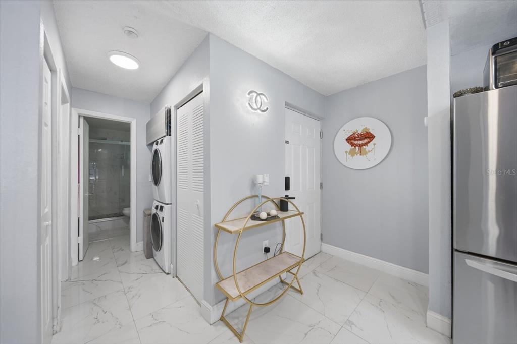 A laundry area with stacked appliances, a gold console table, and a circular wall art piece — 11566 7TH LANE N UNIT 1208, ST PETERSBURG, FL