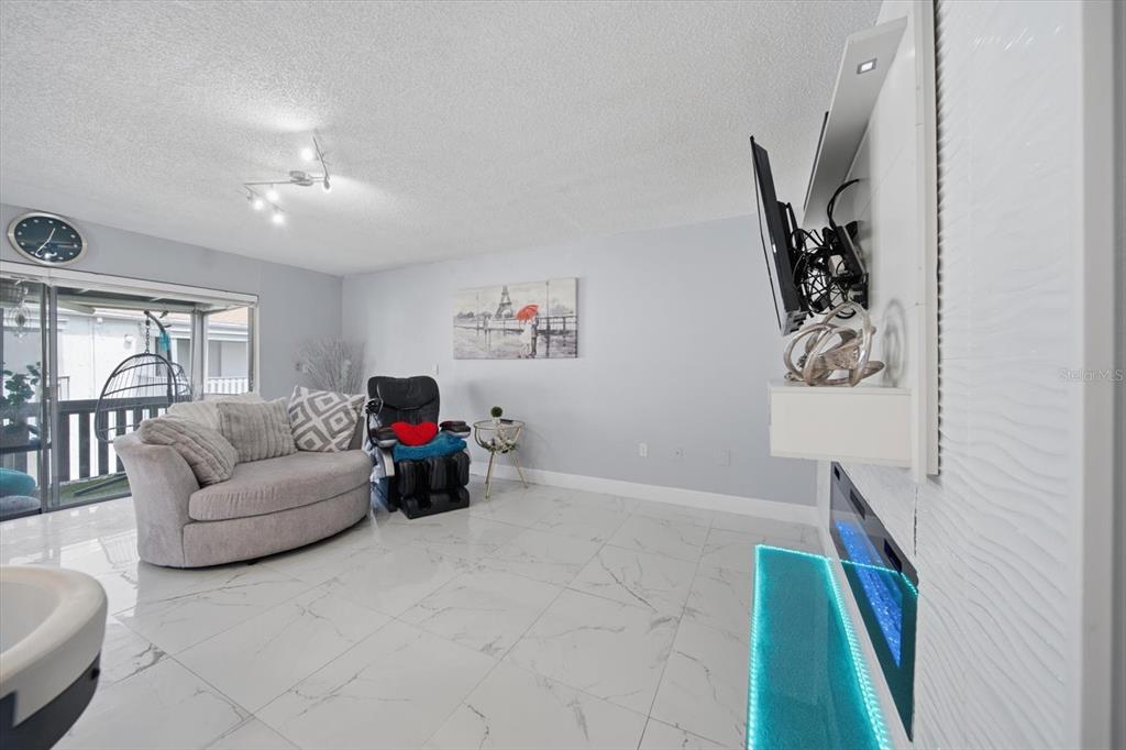 A living room features white tile flooring, a wall-mounted television, and a fireplace — 11566 7TH LANE N UNIT 1208, ST PETERSBURG, FL