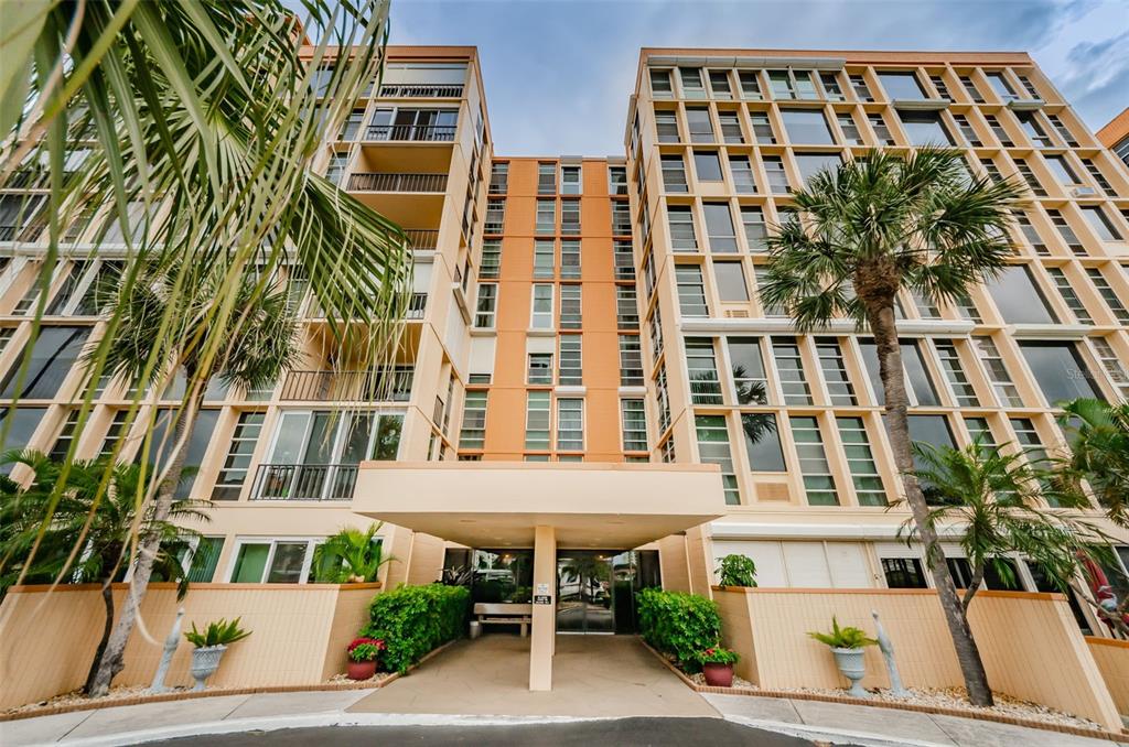 A low-angle view of the exterior entrance to a multi-story tan apartment building — 7400 SUN ISLAND DRIVE S UNIT 806, SOUTH PASADENA, FL