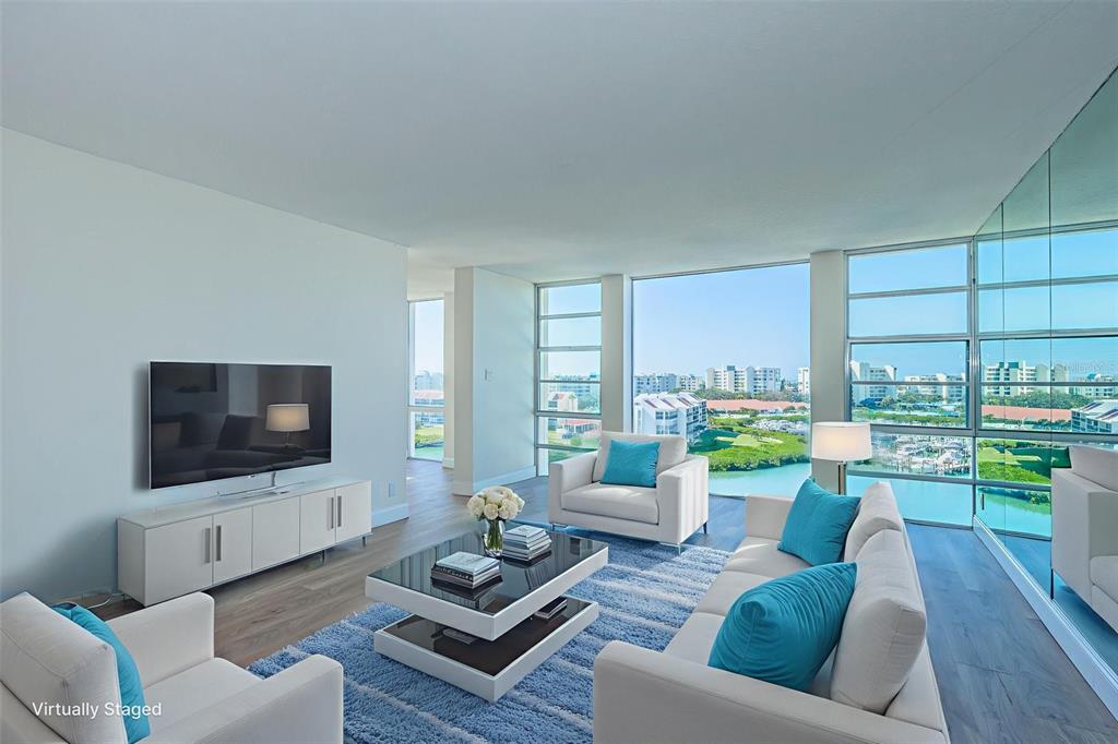 A living room features white furniture, a blue rug, and floor-to-ceiling windows overlooking a marina — 7400 SUN ISLAND DRIVE S UNIT 806, SOUTH PASADENA, FL