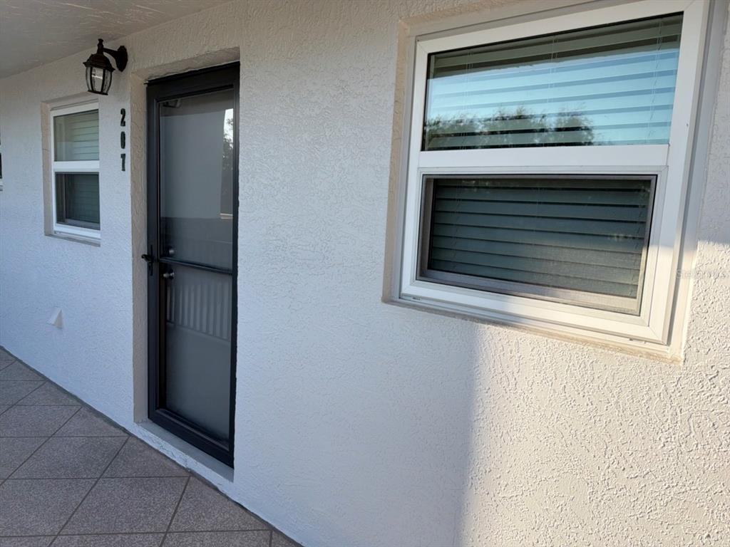 The exterior view shows a white stucco wall with a door numbered 201 and windows — 9815 47TH AVENUE N UNIT 207, ST PETERSBURG, FL