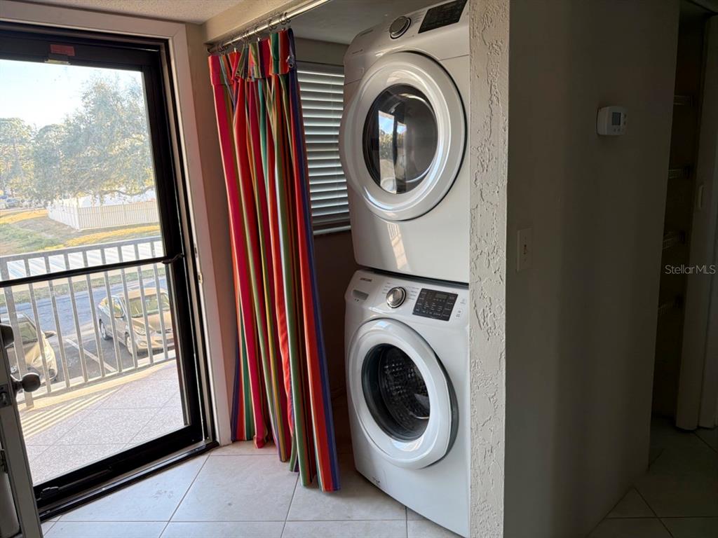 A stacked washer and dryer unit stands next to a sliding glass door with colorful curtains — 9815 47TH AVENUE N UNIT 207, ST PETERSBURG, FL