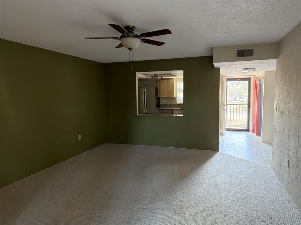 A living room with olive green walls, beige carpeting, a ceiling fan, and a kitchen pass-through — 9815 47TH AVENUE N UNIT 207, ST PETERSBURG, FL