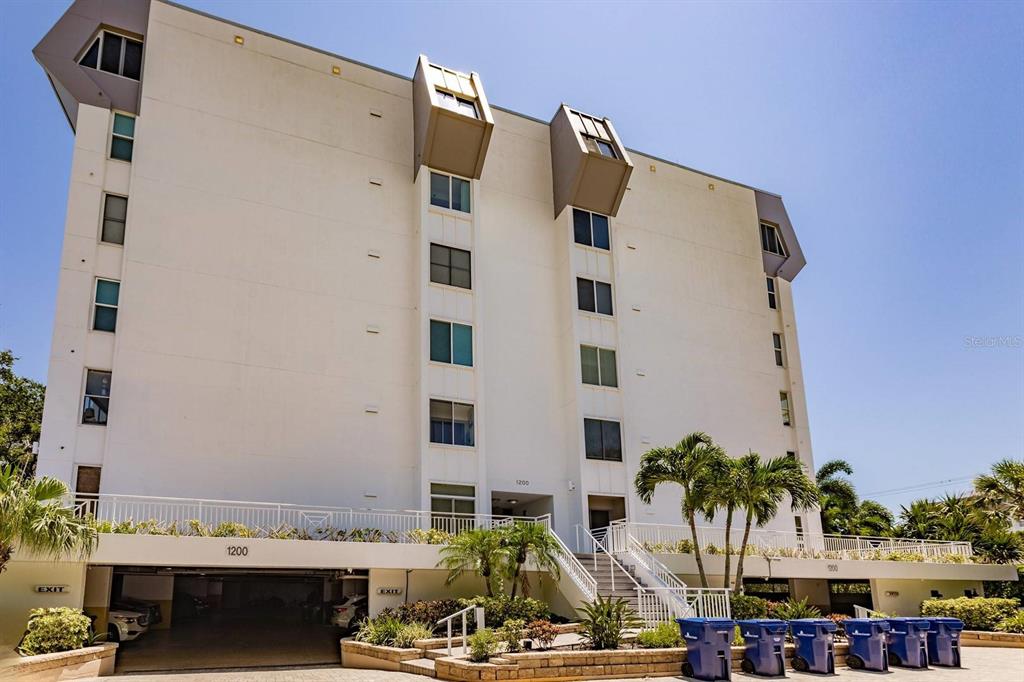 A multi-story white apartment building with a ground-level parking garage and exterior staircases — 1200 E PEPPERTREE LANE UNIT 402, SARASOTA, FL