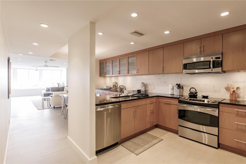 A modern kitchen with light wood cabinets, stainless steel appliances, and a black countertop — 1200 E PEPPERTREE LANE UNIT 402, SARASOTA, FL
