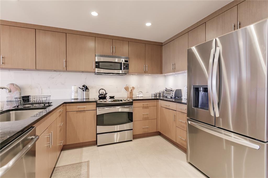 A modern kitchen features light wood cabinets, stainless steel appliances, and white marble-look countertops — 1200 E PEPPERTREE LANE UNIT 402, SARASOTA, FL