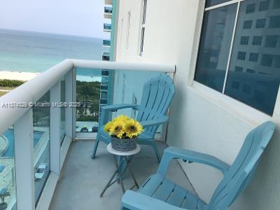 A balcony with two light blue chairs and a small table holding yellow flowers — 9201 Collins Ave # 921, Surfside FL 33154, SURFSIDE, FL