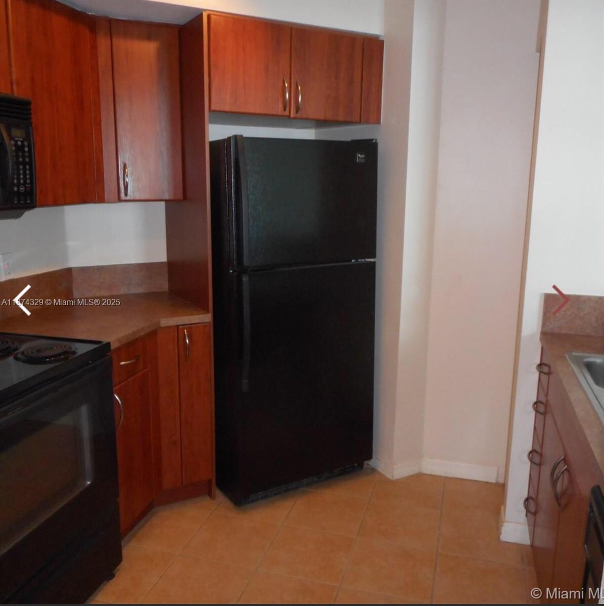 A kitchen features wood cabinets, a black refrigerator, a black stove, and tiled flooring — 9201 Collins Ave # 921, Surfside FL 33154, SURFSIDE, FL