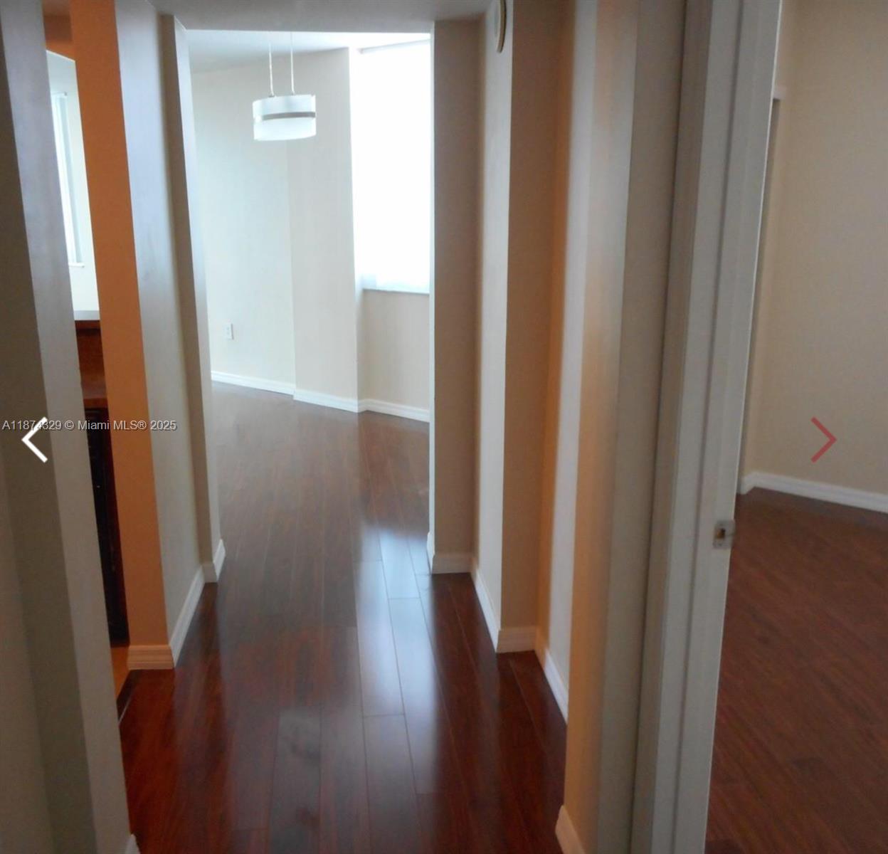 A hallway with dark wood flooring leads to an open living area with a pendant light — 9201 Collins Ave # 921, Surfside FL 33154, SURFSIDE, FL