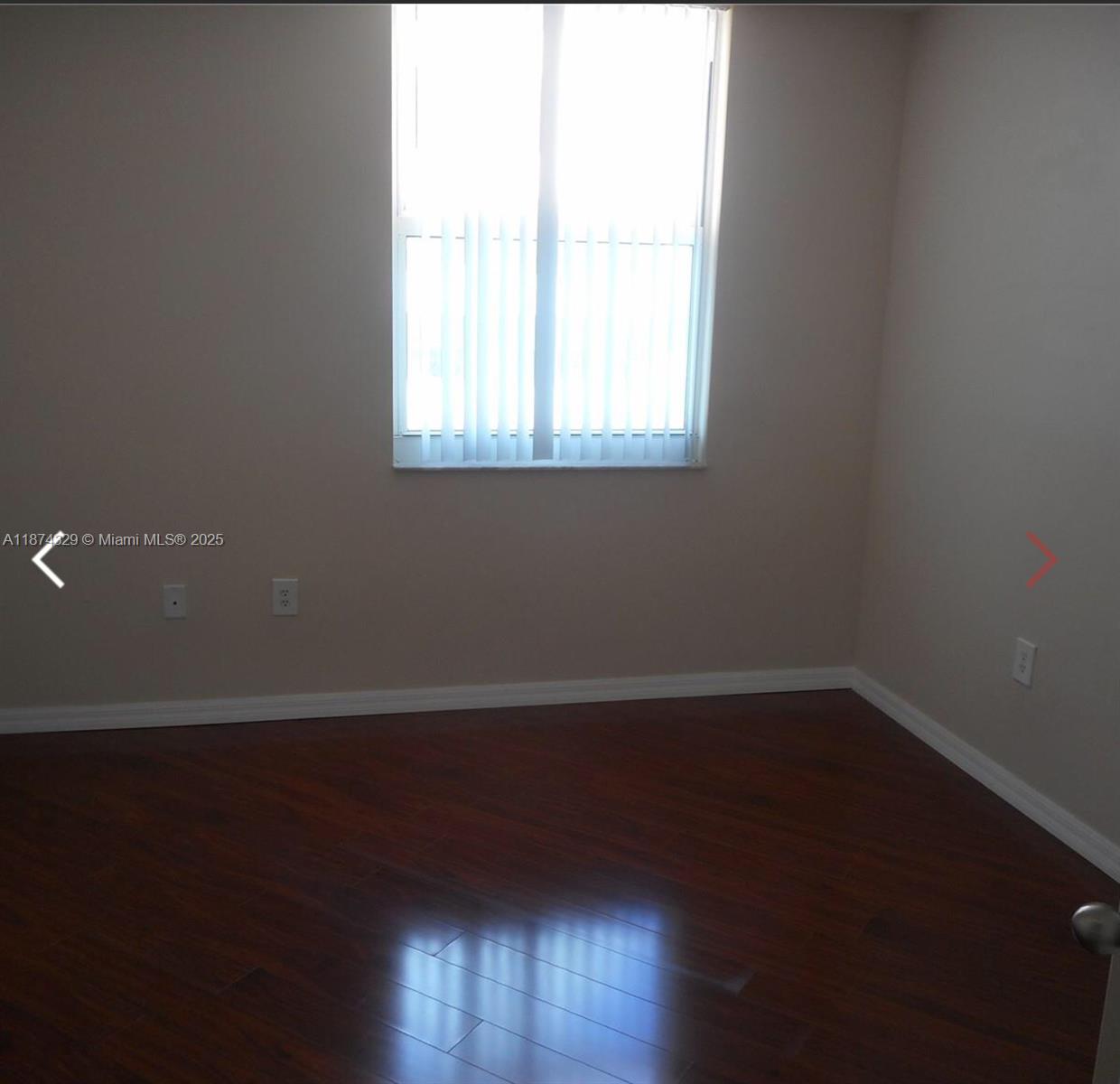 An empty room features dark wood flooring, beige walls, and a window with vertical blinds — 9201 Collins Ave # 921, Surfside FL 33154, SURFSIDE, FL