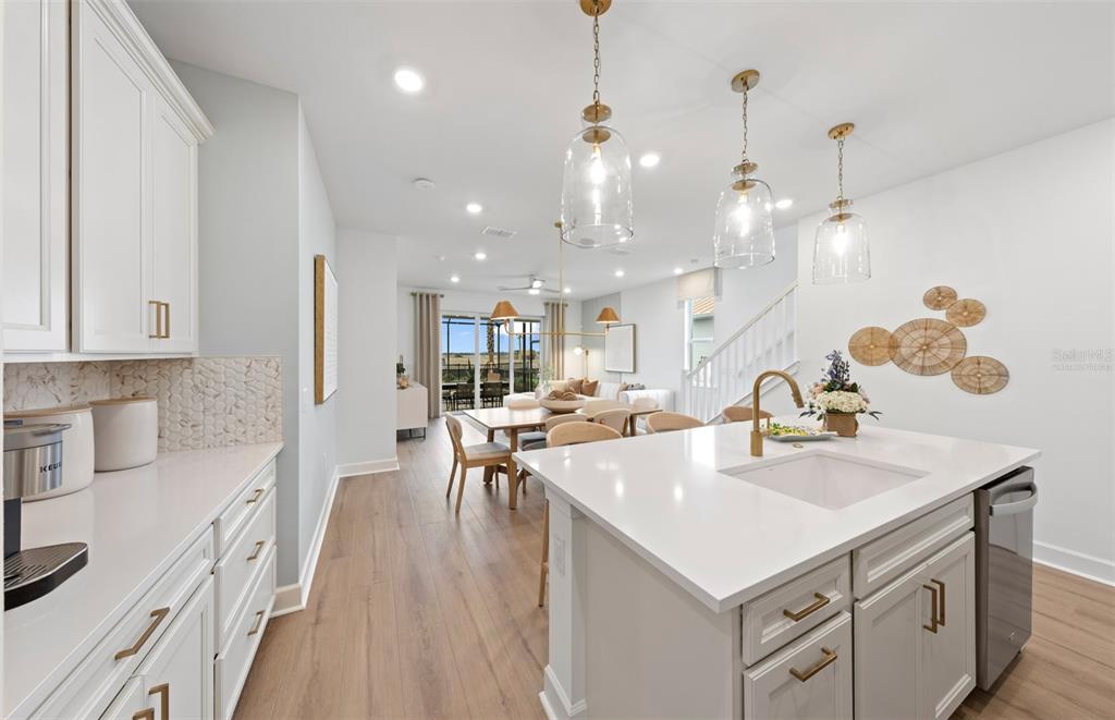 A bright kitchen with white cabinets, a quartz island, and wood-look flooring leads to dining — 84 LAKE MANATEE DRIVE, PALM COAST, FL