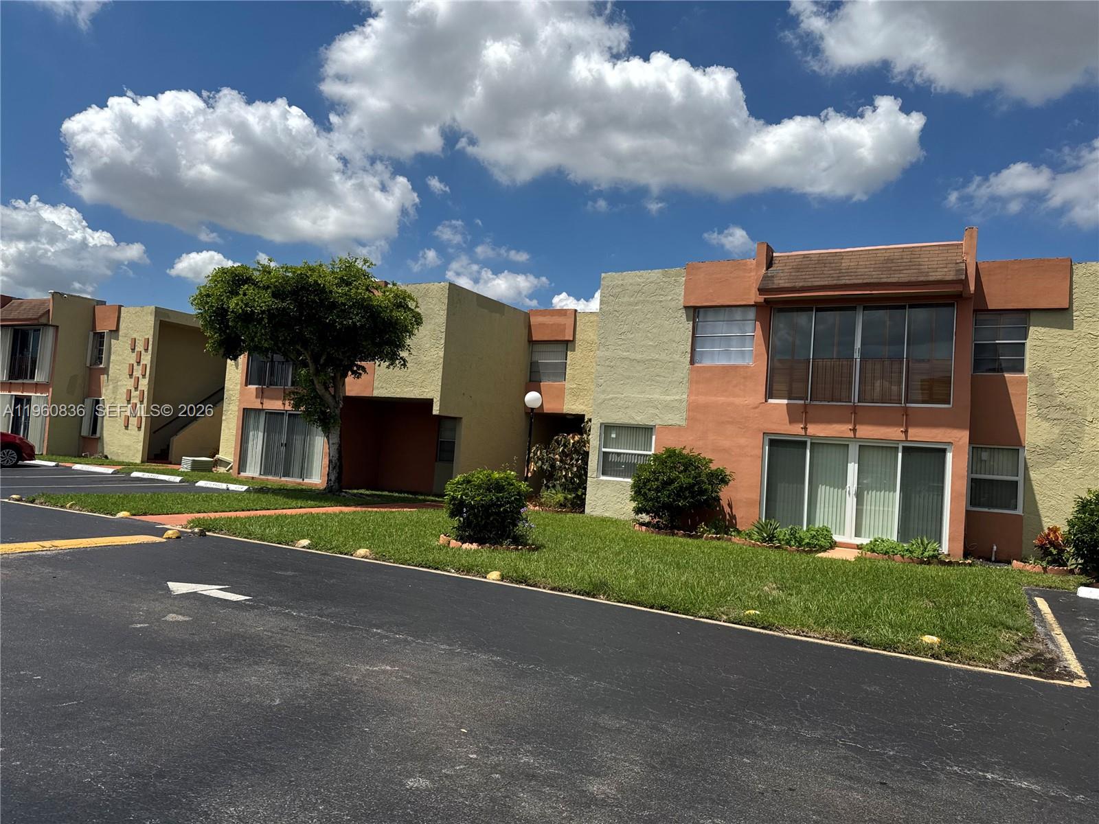 A two-story apartment building features tan and orange stucco walls under a blue sky — 9350 W Flagler St # 105A, Miami FL 33174, MIAMI, FL