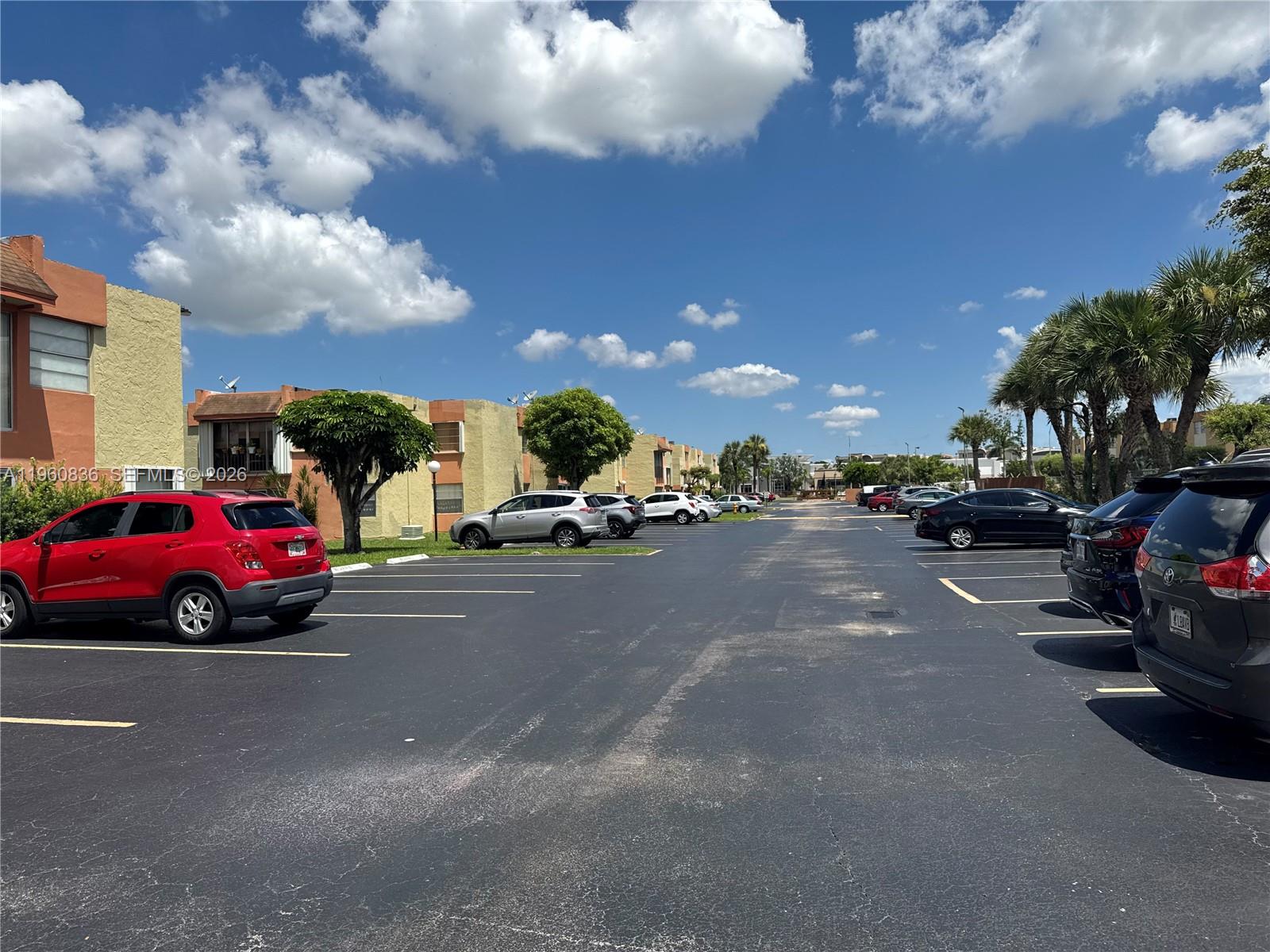 A parking lot sits between two-story apartment buildings under a bright, partly cloudy sky — 9350 W Flagler St # 105A, Miami FL 33174, MIAMI, FL