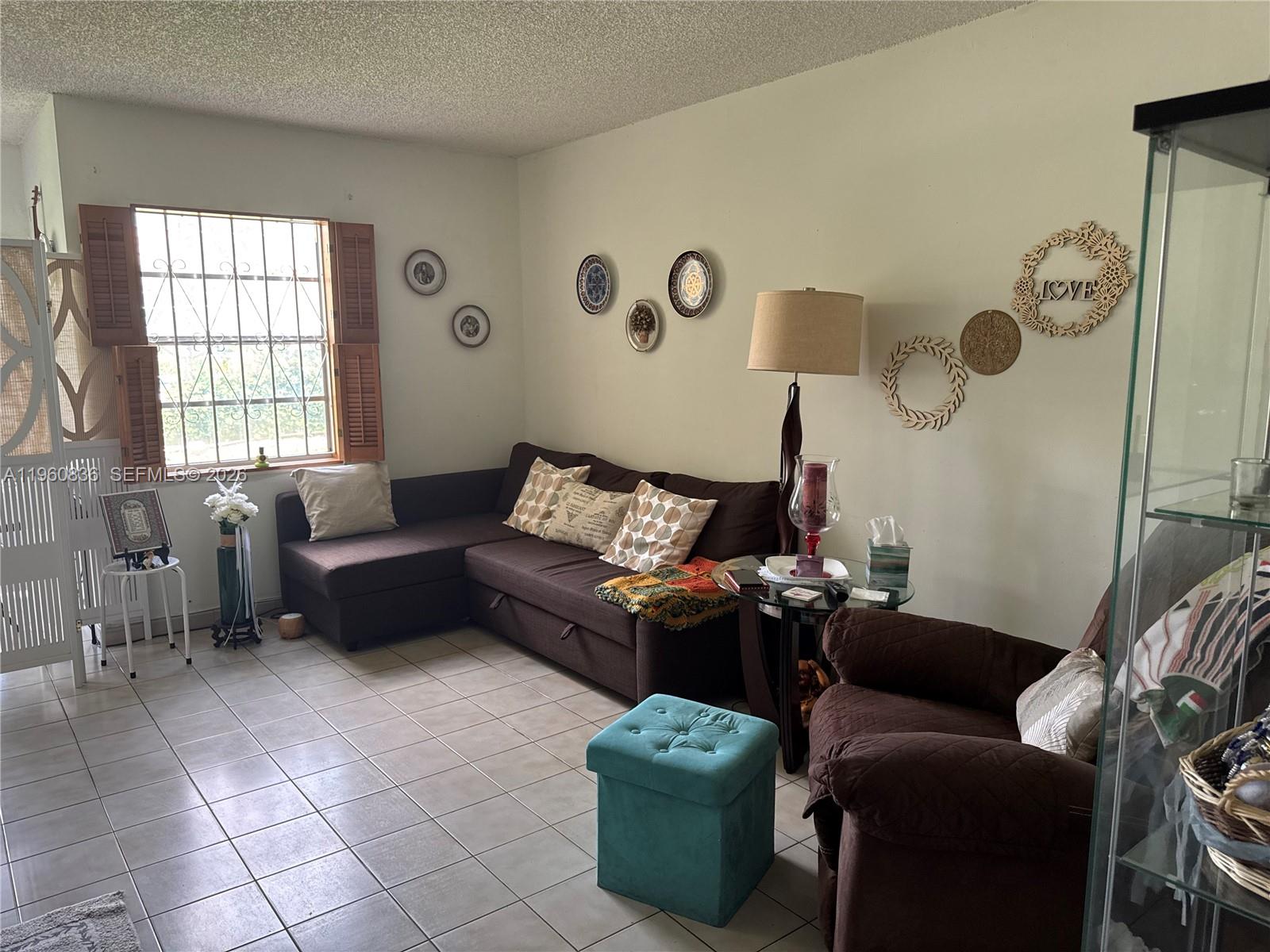 A living room features a brown sectional sofa, a teal ottoman, and wall-mounted decorative accents — 9350 W Flagler St # 105A, Miami FL 33174, MIAMI, FL