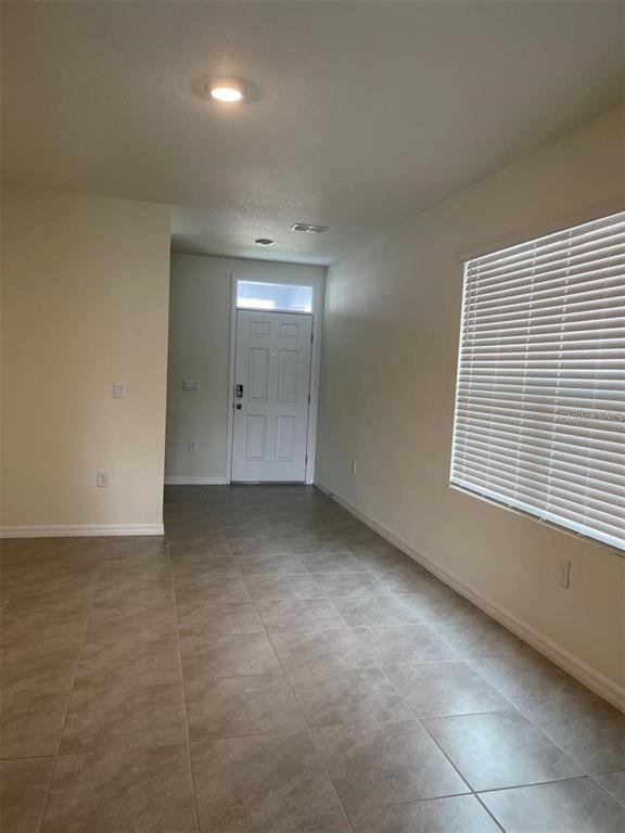 A room with light-colored tile flooring, a white front door, and a window with blinds — 5526 OXFORD GRAY ROAD, WESLEY CHAPEL, FL
