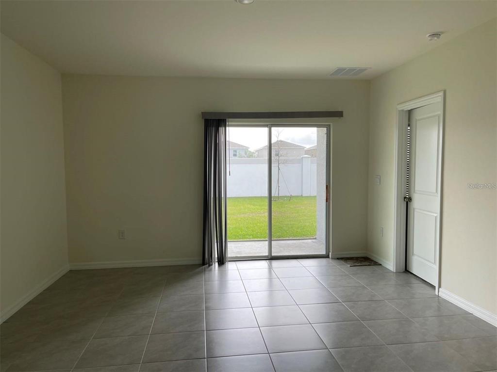 An empty room with gray tile flooring, a sliding glass door, and a white door — 5526 OXFORD GRAY ROAD, WESLEY CHAPEL, FL