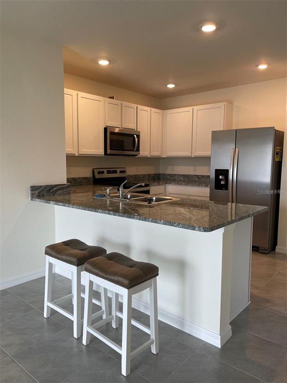 A kitchen with white cabinets, granite countertops, stainless steel appliances, and two bar stools — 5526 OXFORD GRAY ROAD, WESLEY CHAPEL, FL