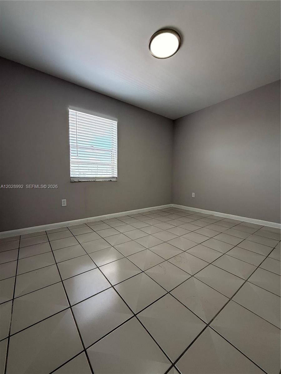 An empty room features gray walls, white baseboards, a single window, and light-colored tiled flooring — 6820 W Flagler St # 407, Miami FL 33144, MIAMI, FL