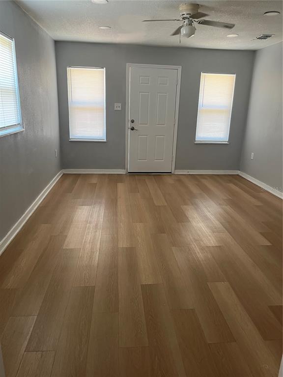 A room with light wood-look flooring, gray walls, two windows, and a white entry door — 1424 N TREMAIN STREET, MOUNT DORA, FL