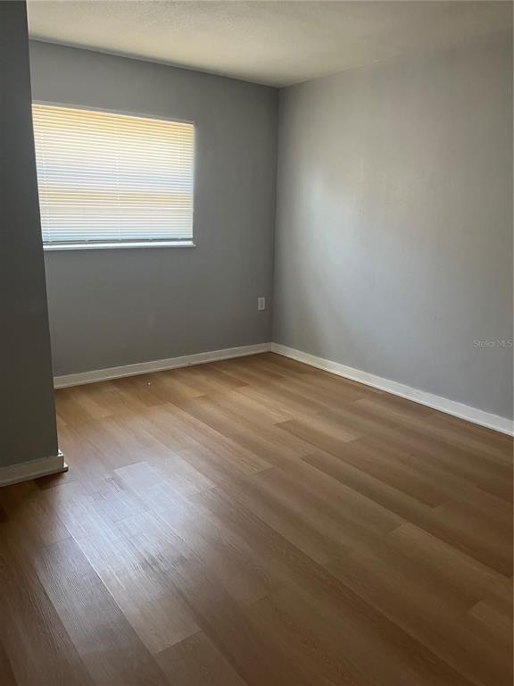 An empty bedroom features light gray walls, wood-look flooring, and a window with white blinds — 1424 N TREMAIN STREET, MOUNT DORA, FL