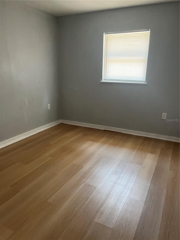 An empty room features light-colored wood-look flooring, grey walls, and a single window with blinds — 1424 N TREMAIN STREET, MOUNT DORA, FL