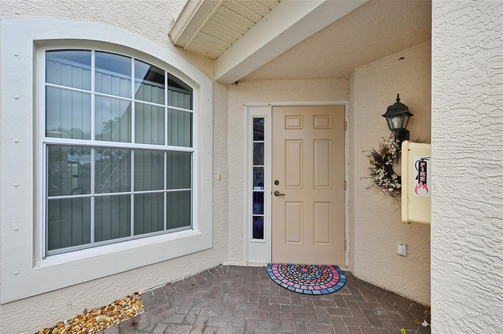 A beige front door with a sidelight and arched window sits on a brick patio — 7050 PROSPERITY CIRCLE UNIT 904, SARASOTA, FL