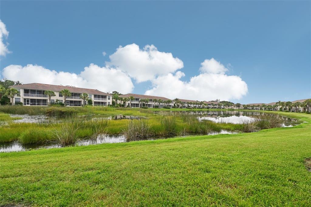 A multi-story apartment complex overlooks a pond surrounded by grassy lawns and reeds — 7050 PROSPERITY CIRCLE UNIT 904, SARASOTA, FL